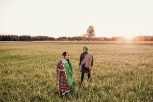 A couple in colorful traditional clothing stands together in a golden field at sunset.