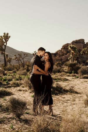Intimate desert engagement photo with Joshua trees and rocky terrain in the background.