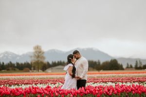 A romantic moment between two figures standing in a vibrant red tulip field with mountains in the background.