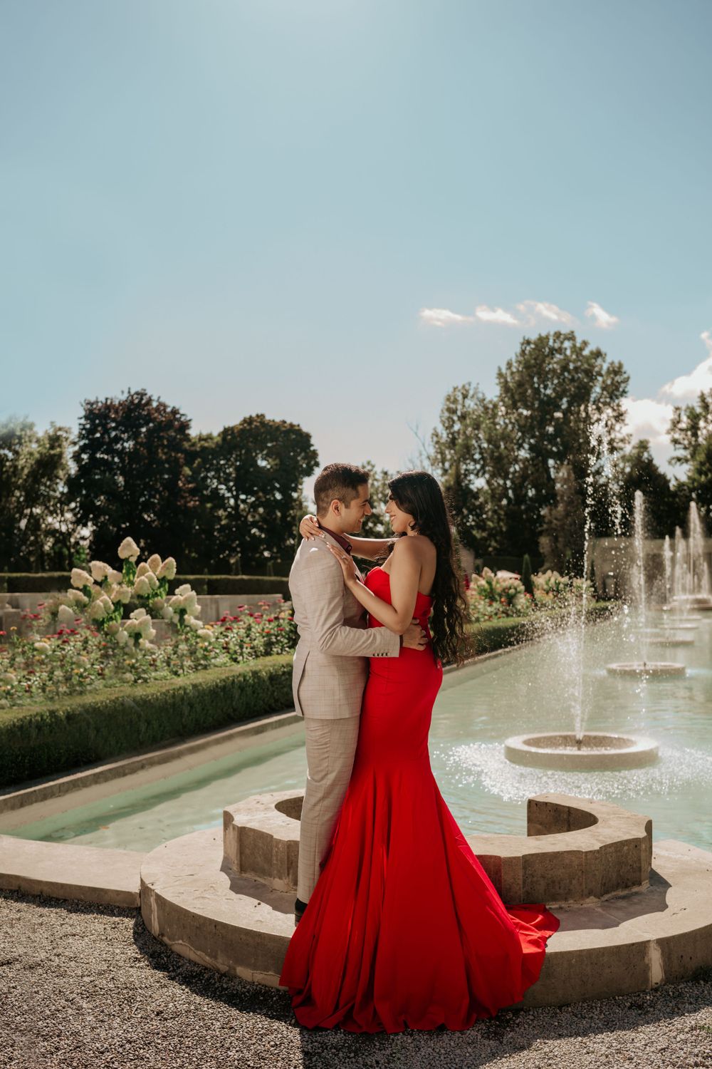 Elegant couple shares an intimate moment by a stone fountain in a manicured garden setting.