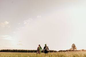 A couple holds hands while walking through a sunlit meadow at golden hour.