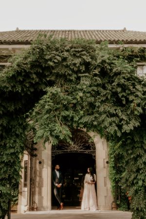 A couple poses in a dramatic ivy-covered stone archway entrance.