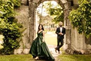 A romantic engagement photo featuring an emerald green gown against a stone archway covered in lush ivy.