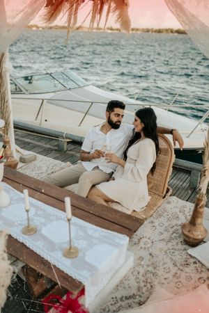 Couple lounging on luxury yacht deck with romantic sunset lighting and flowing fabric decor.