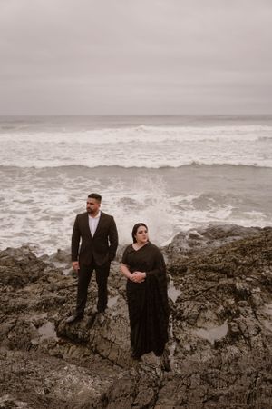Dramatic coastal photoshoot on rocky cliffs overlooking stormy ocean waves.