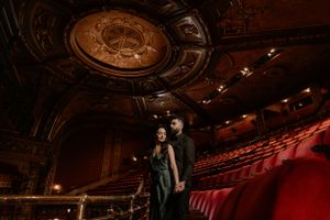Dramatic theater interior shot showcasing ornate ceiling details and rows of red seats.