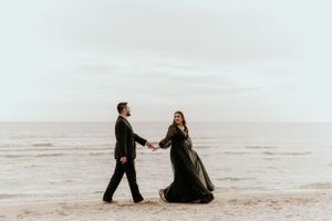Couple walks hand in hand along a misty beach in formal attire.