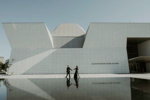 Two silhouettes reflected in water in front of modern white architectural building.