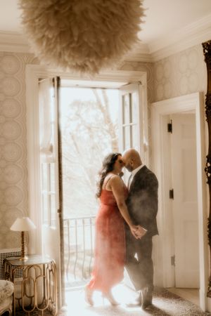 Romantic sepia-toned photo of couple embracing in sunlit doorway beneath decorative ceiling fixture.