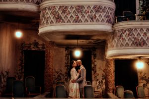 Couple shares an intimate moment in an ornate vintage theater with decorative columns.