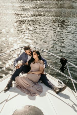 Romantic couple relaxing on bow of boat during sunset across rippling water.