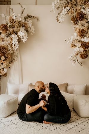 Intimate moment captured on white couch with dried floral arrangements decorating the wall.