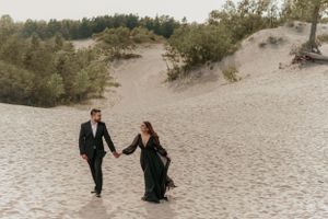 A couple walks hand in hand through sandy dunes on a romantic desert photoshoot.