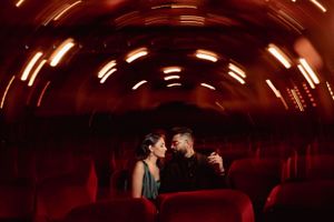 Romantic couple seated in dimly lit theater with curved ceiling and dramatic red lighting.