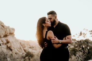A romantic couple embrace against a rocky desert landscape at sunset.