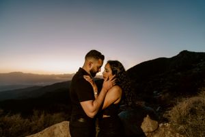 A couple shares an intimate sunset moment on a mountain overlook.