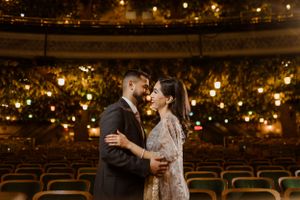 Couple embracing in elegant theater with glowing lights in background.