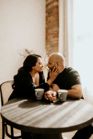 Cozy coffee date scene at small cafe table with exposed brick wall and natural lighting.