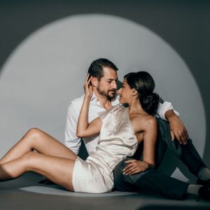 Intimate couple portrait with dramatic lighting and minimalist studio backdrop.