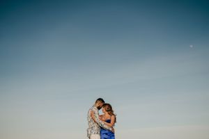 Romantic couple embracing against blue sky in elegant attire.