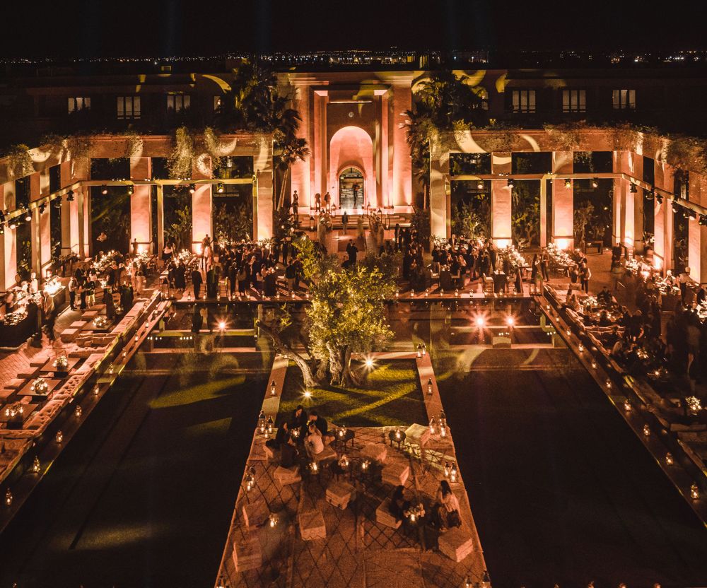 Romantic outdoor wedding reception with long tables and string lights in a columned courtyard.