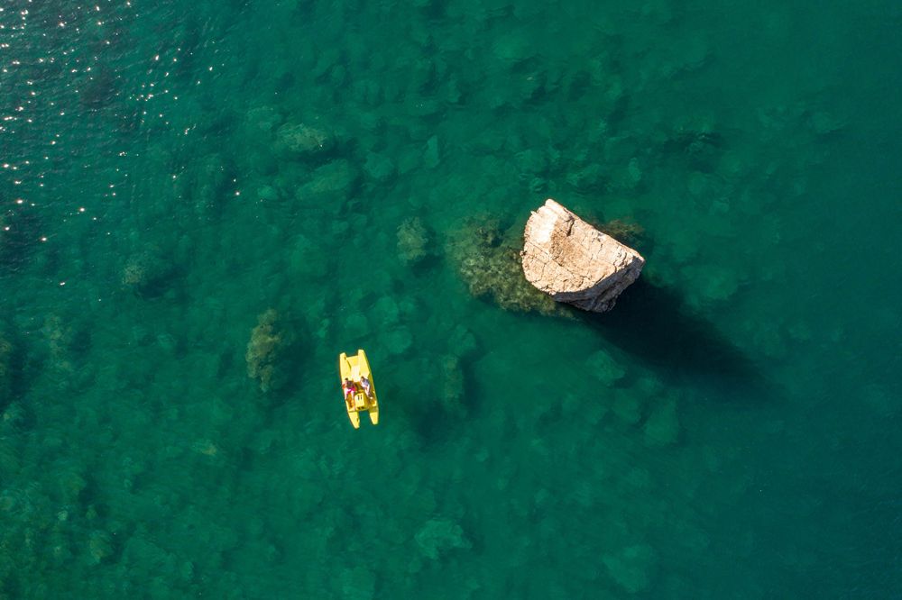 Aerial view of a yellow float and large rock formation in crystal clear turquoise waters.
