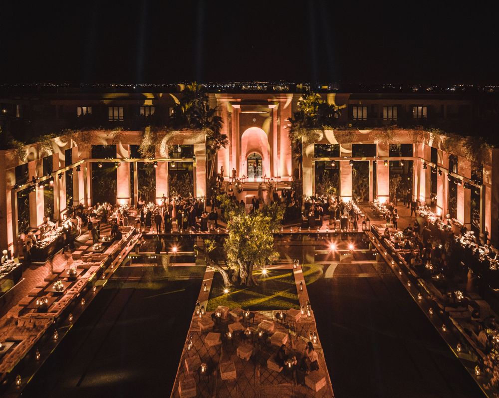An elegant evening wedding reception setup in a grand courtyard with ornate columns and warm lighting.