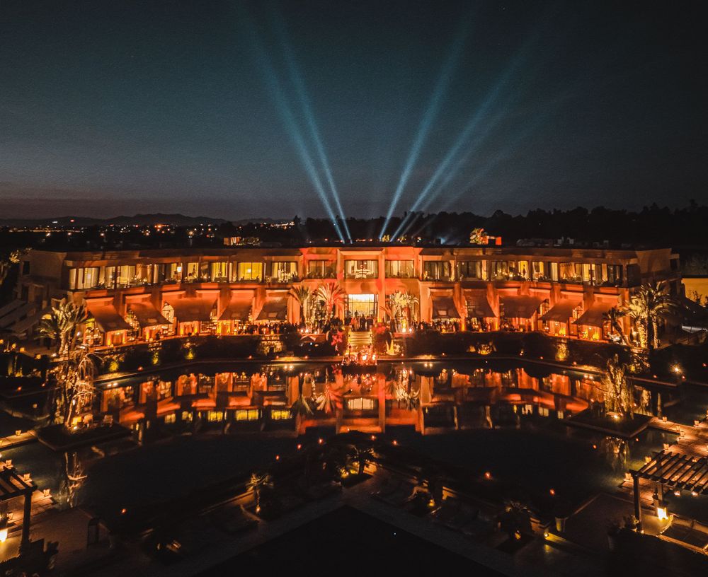 Multi-level resort building illuminated at night with dramatic blue spotlights shooting skyward.