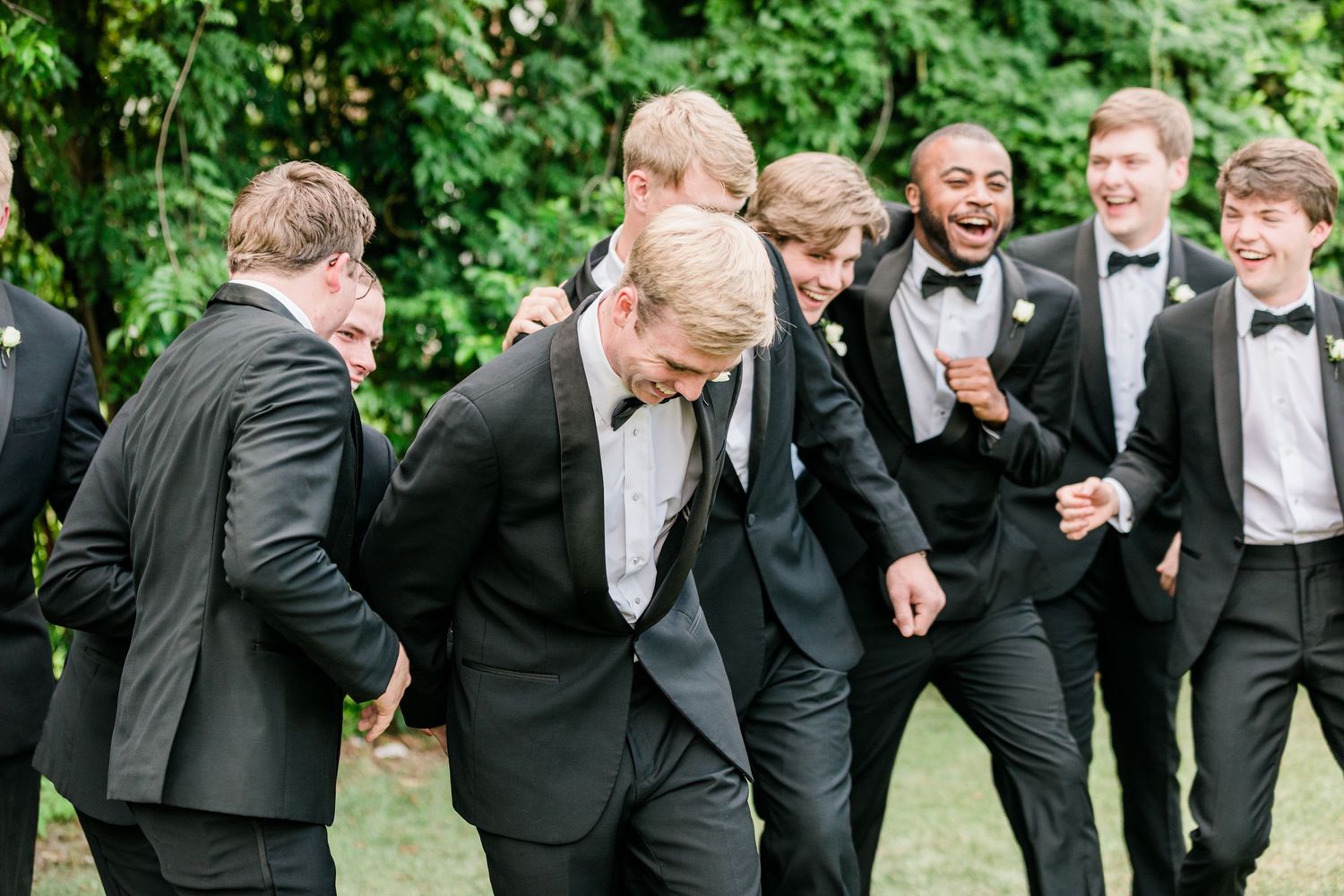 Groomsmen in tuxedos share a candid laughing moment during outdoor wedding photos.