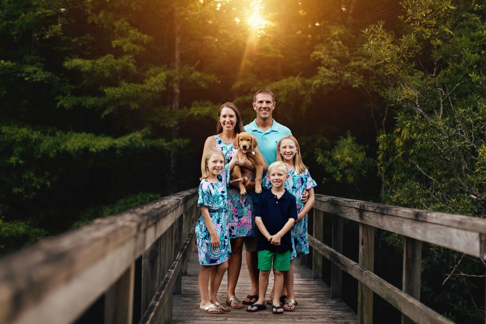A group poses together on a wooden bridge during golden hour in a forest setting.