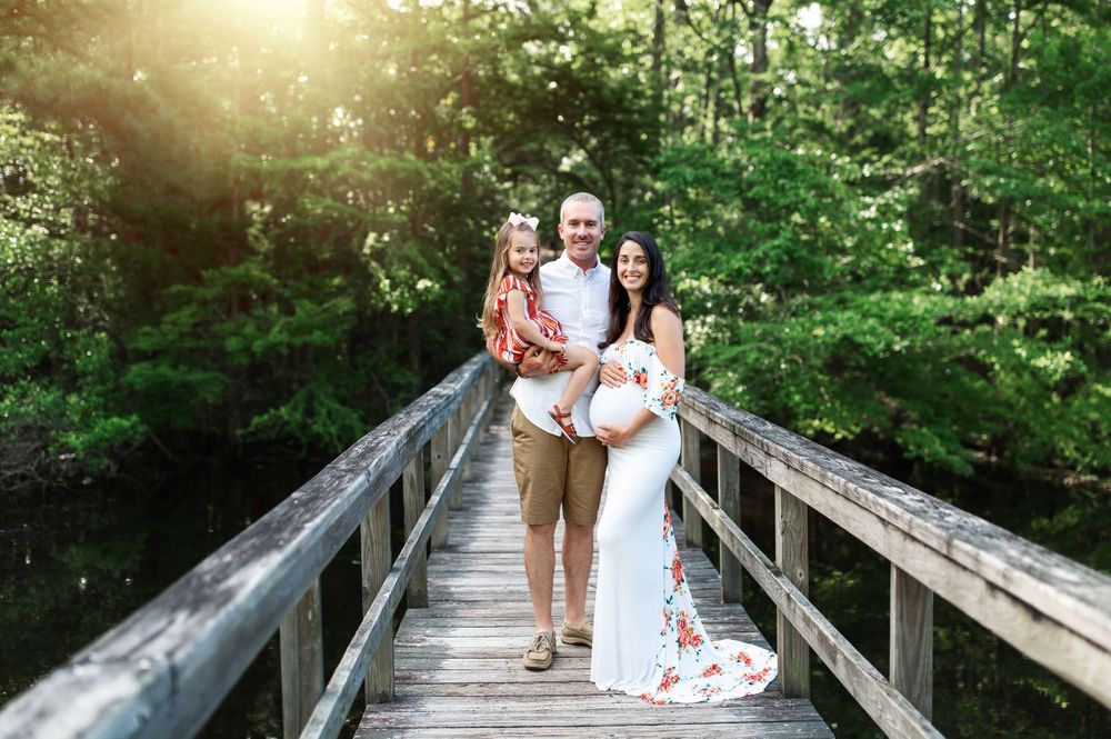 A family poses together on a wooden bridge in a lush green forest setting with golden sunlight.