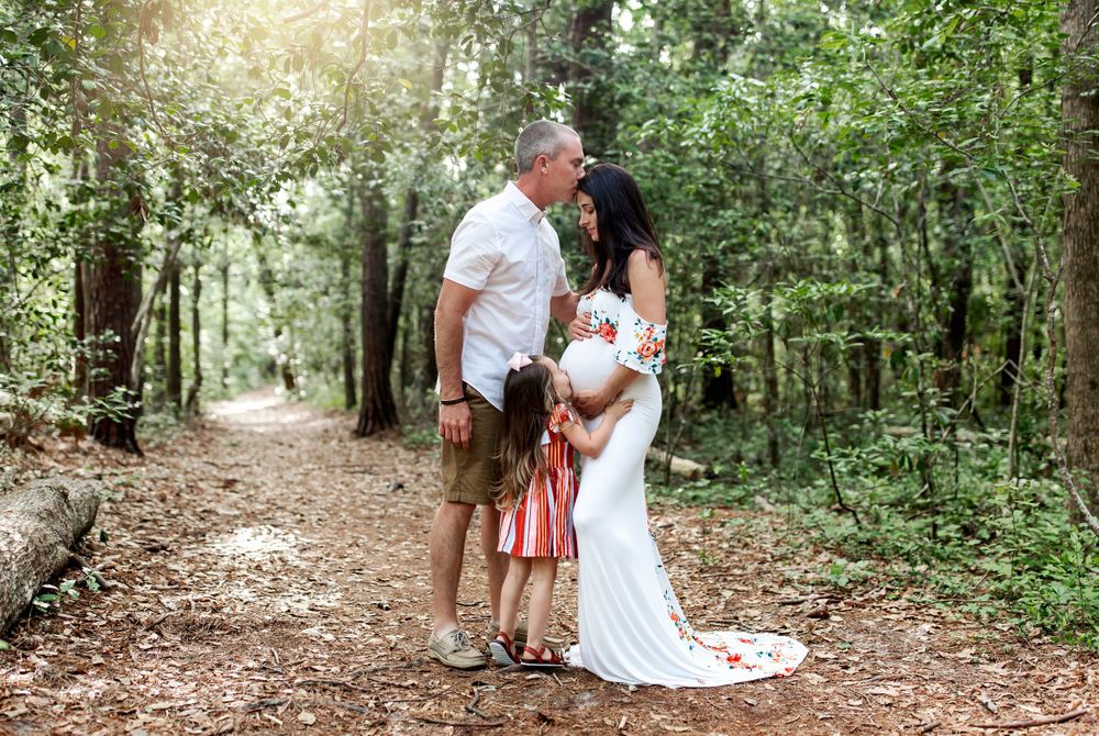 A family stands together on a wooded path with sunlight streaming through the trees.