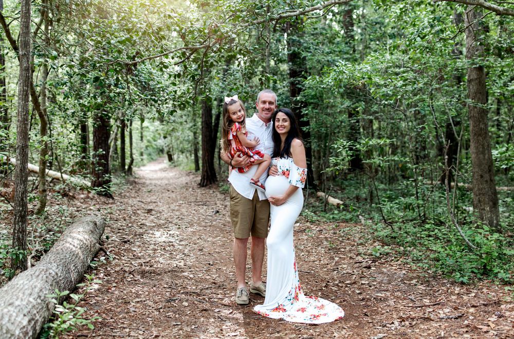 A family poses together on a forest trail surrounded by lush greenery and filtered sunlight.