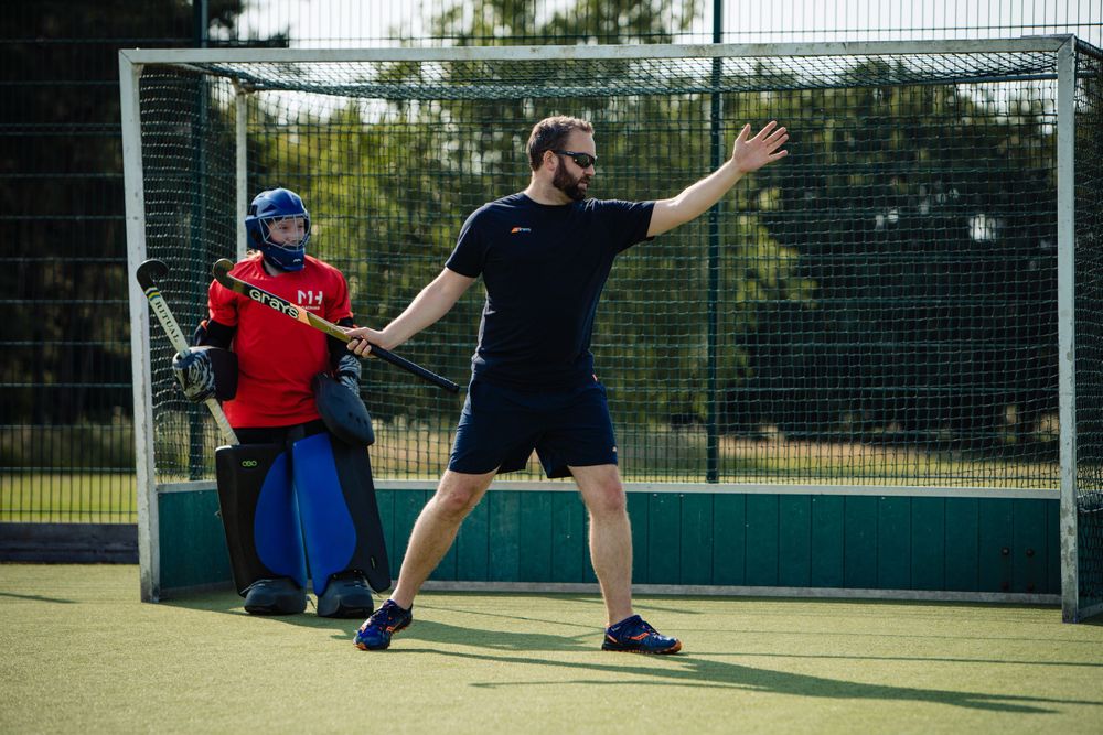 Field hockey coaching session with goalkeeper and trainer on an outdoor pitch
