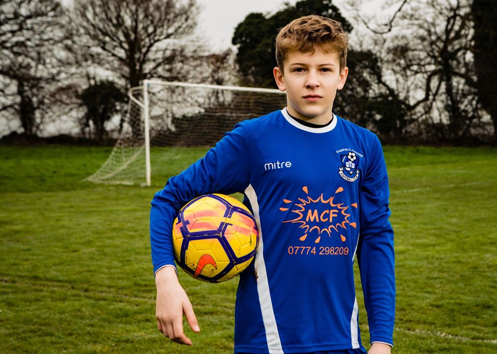 Youth football portrait of a young player holding a football on a grass pitch