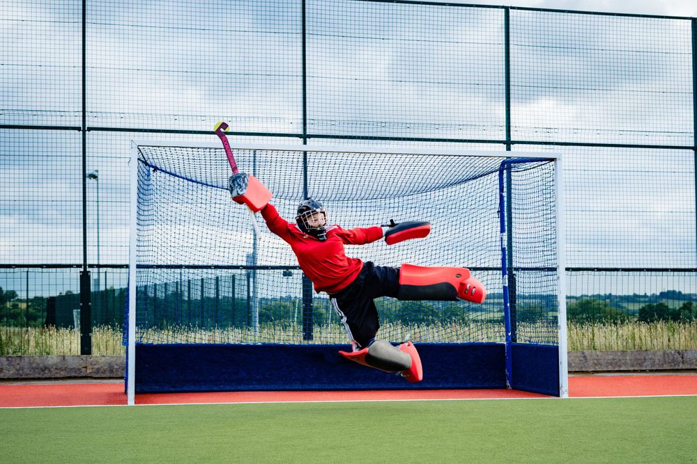 Field hockey goalkeeper diving to save goal during competitive match