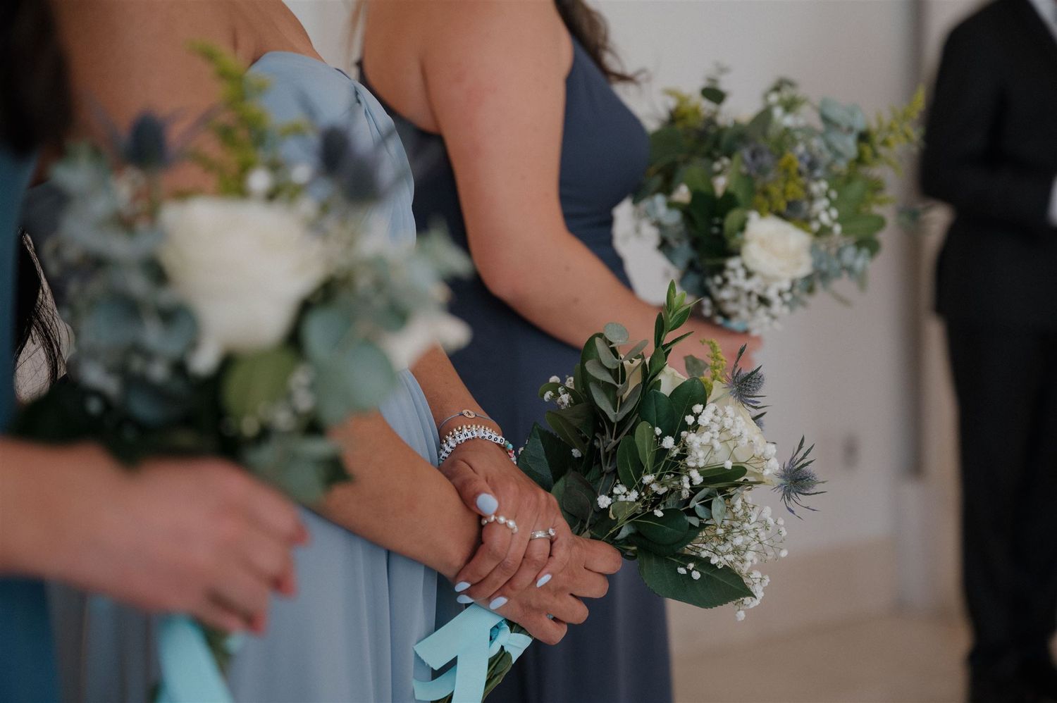 Bridesmaids holding delicate white and green floral bouquets in blue dresses.