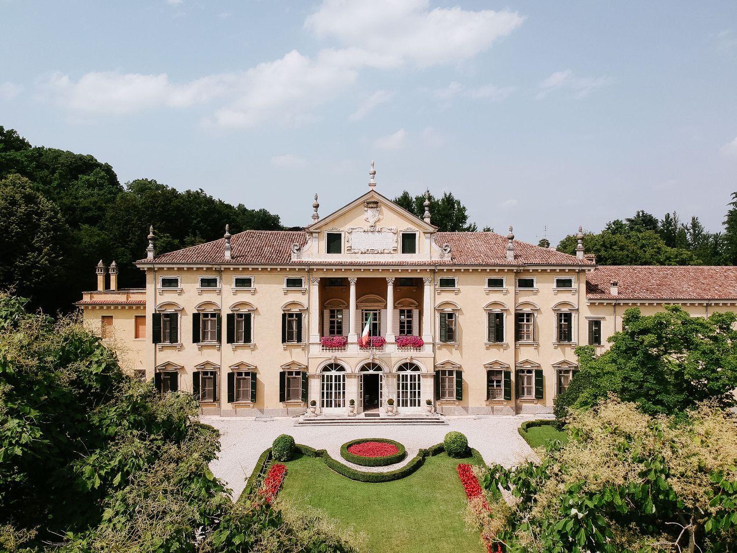Grand Italian villa with neoclassical architecture featuring symmetrical design and manicured front garden.