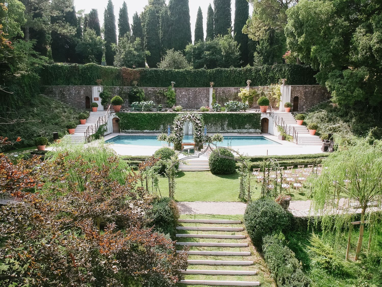 Formal garden with stone steps leading to a rectangular pool flanked by cypress trees and manicured hedges.