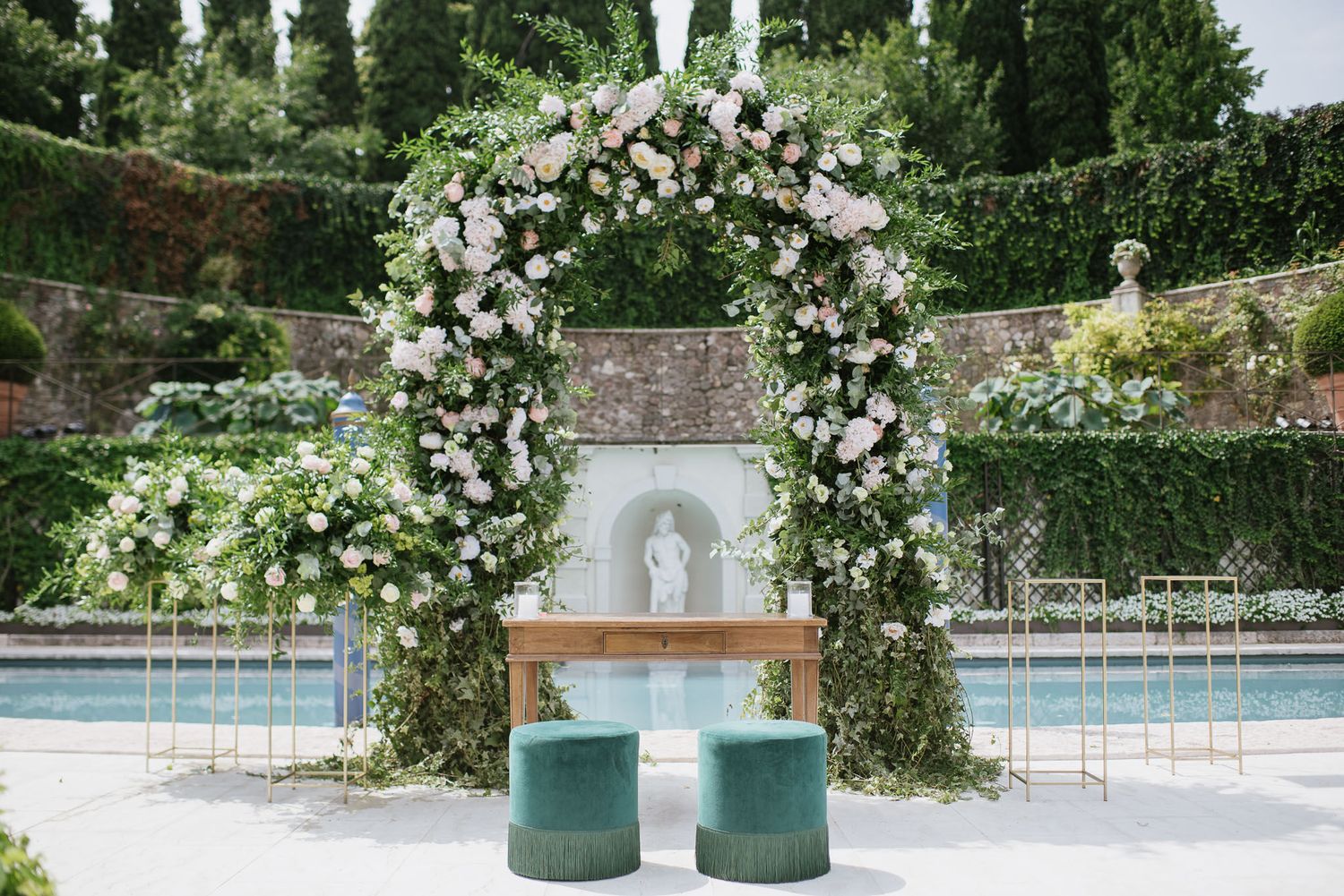 Elegant garden ceremony arch with white florals and teal seating arrangements.