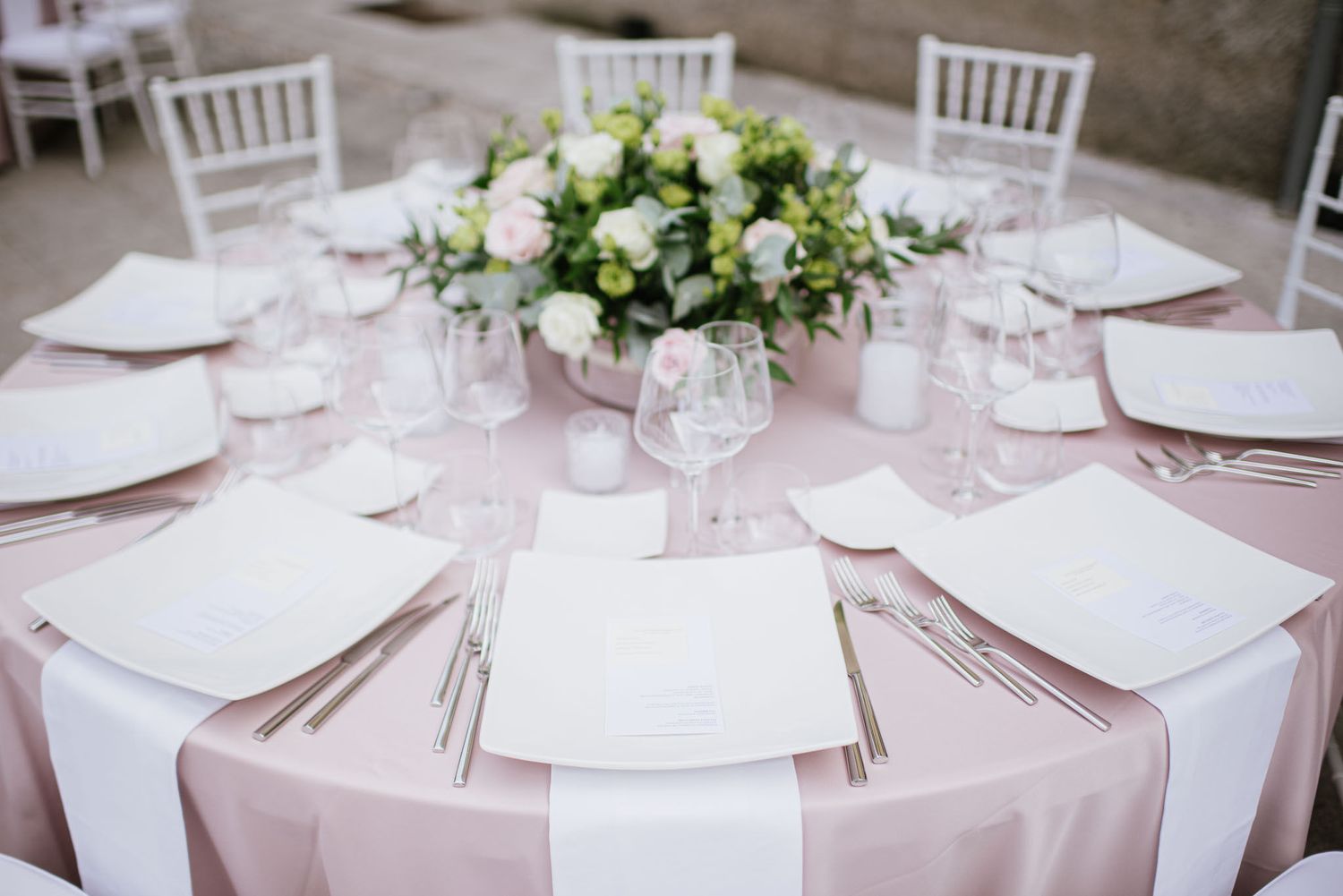 Round dining table set with blush pink linens, white plates and floral centerpiece for an elegant wedding reception.