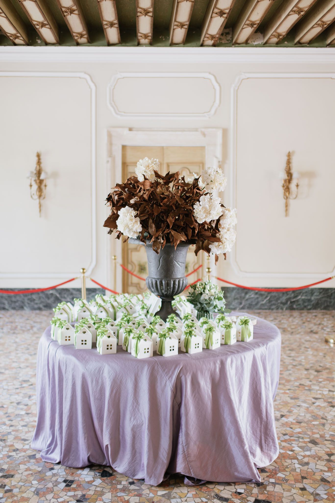 Wedding favor display table with dried floral arrangement and lavender tablecloth in ornate interior.