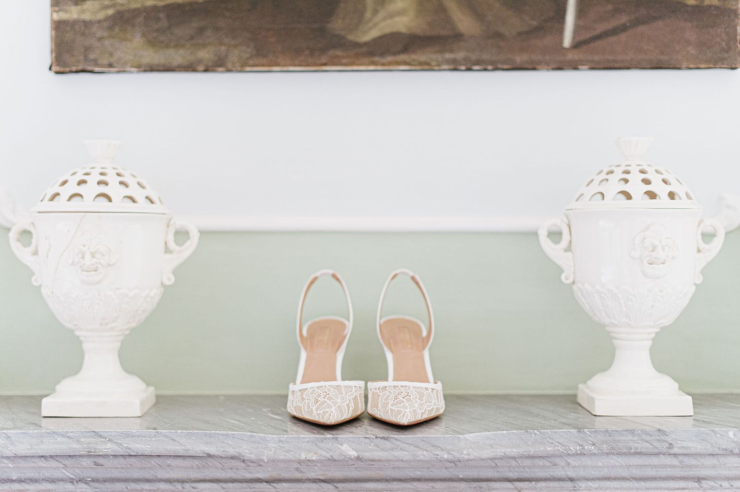 White decorative urns flank elegant bridal shoes on a pale green shelf.
