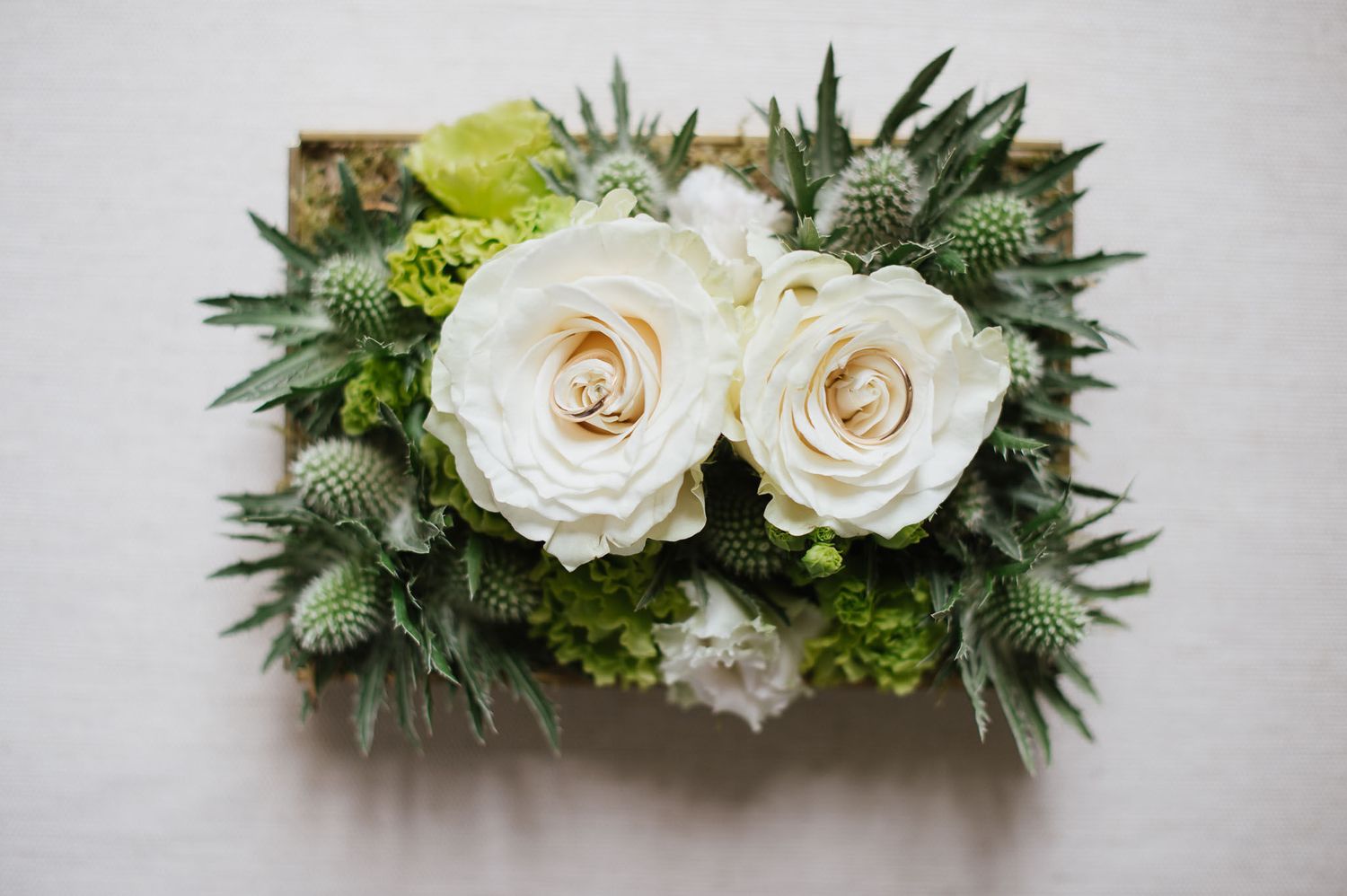 Close-up of white roses and green thistle floral arrangement in rustic style.