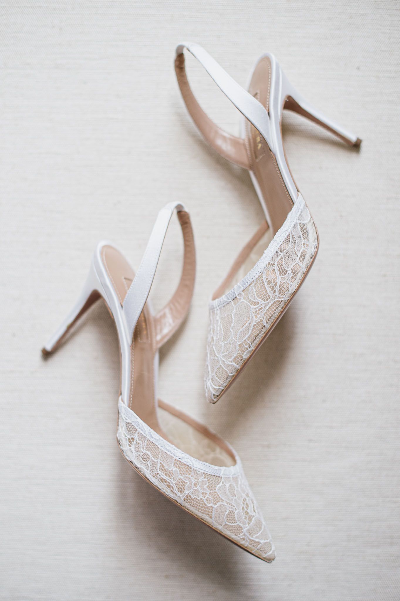 Delicate white lace slingback wedding heels with pointed toe on neutral background.