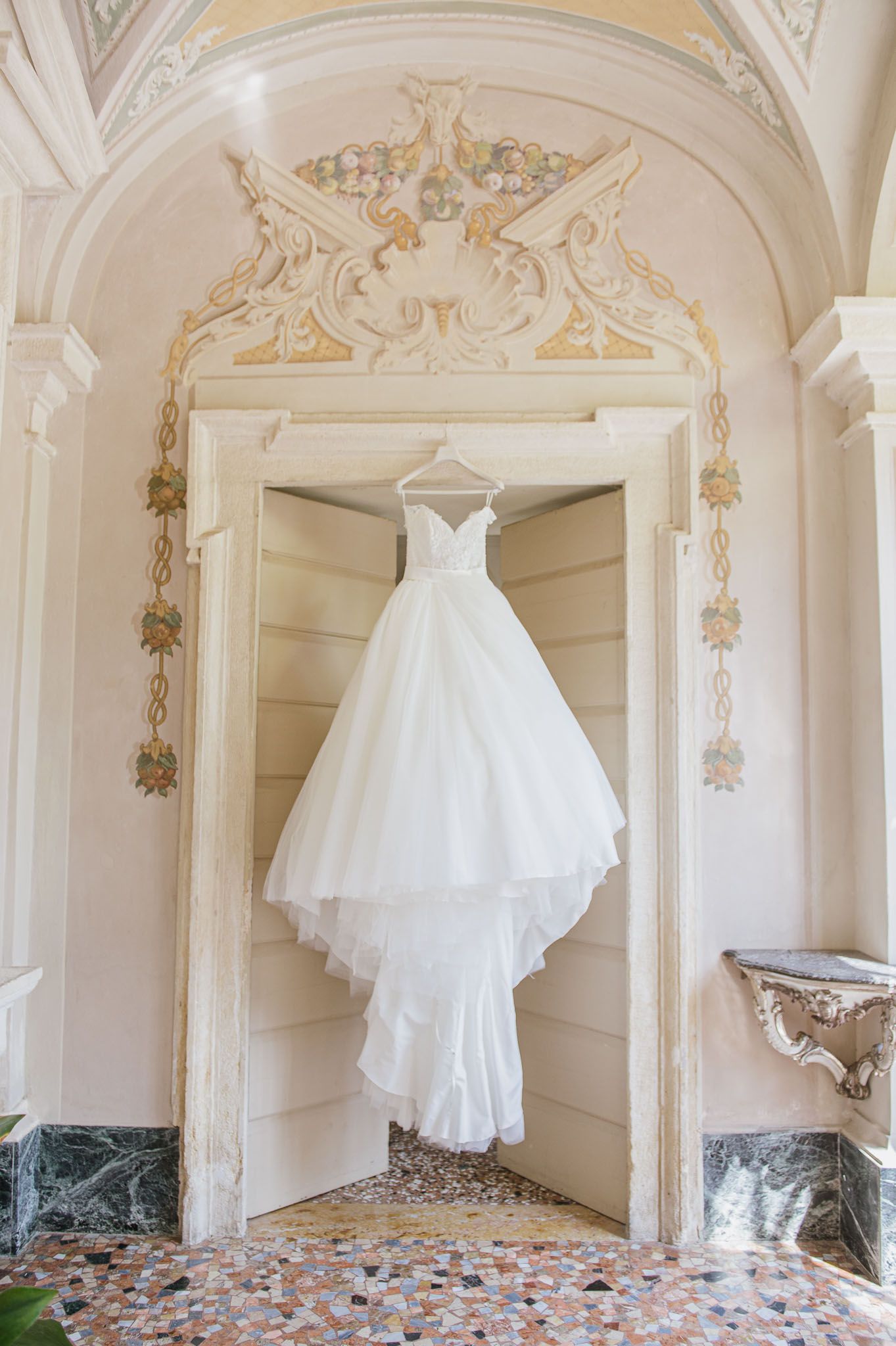 White tulle wedding gown hanging in ornate archway with gold architectural details.