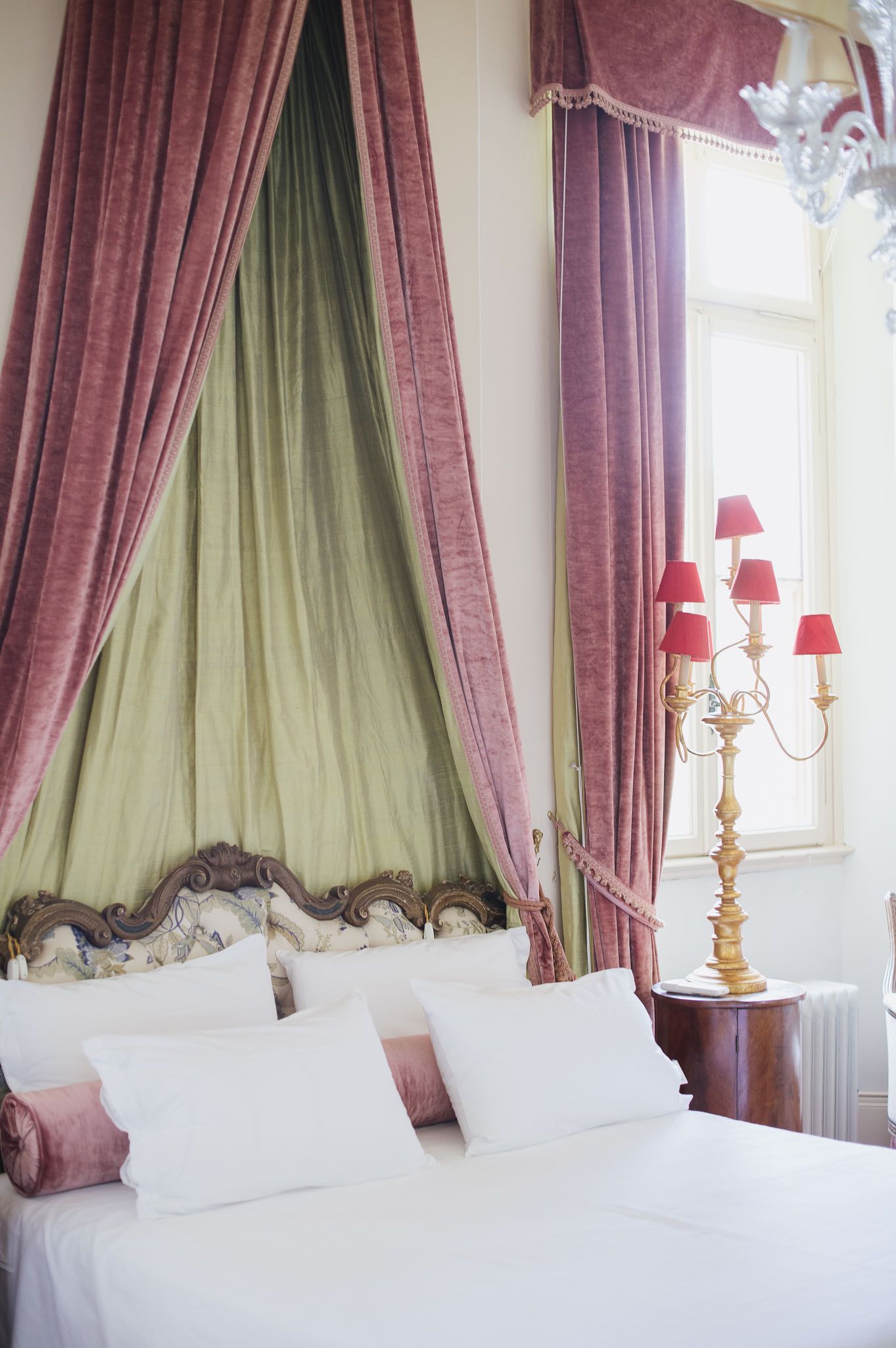 Luxurious bedroom with canopy bed featuring pink and sage green drapes and ornate gold candelabra.