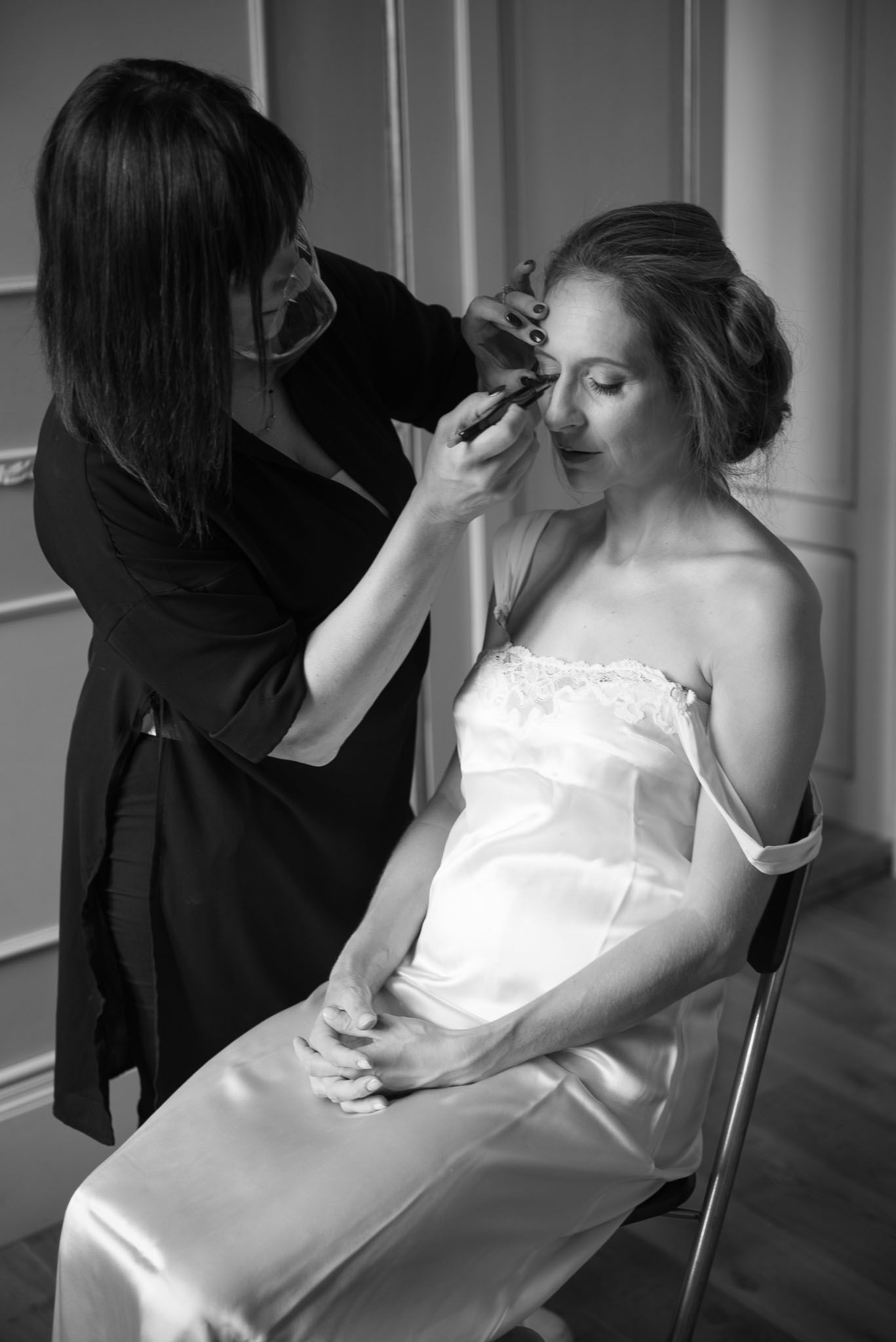 Wedding preparation scene showing final makeup touches being applied in black and white.