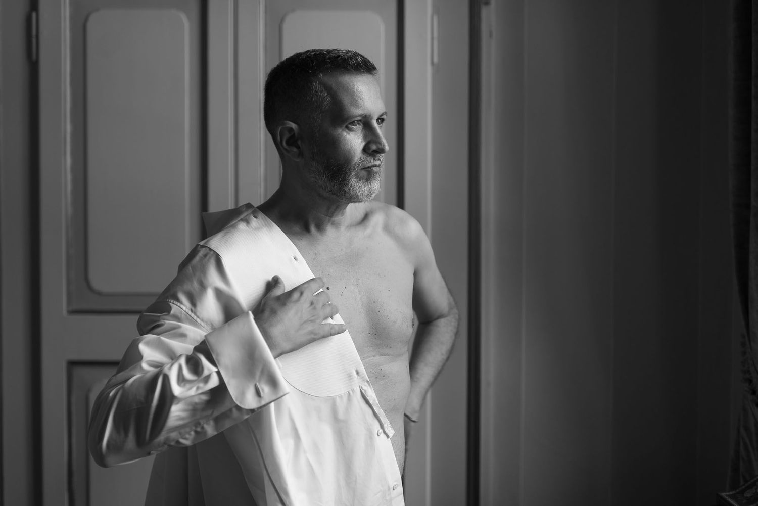 Black and white portrait of someone getting dressed in formal attire by a window.