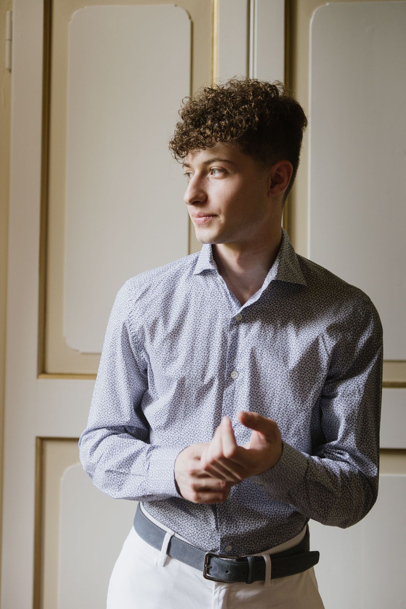 Profile view of someone in a patterned button-down shirt against cream paneled walls.